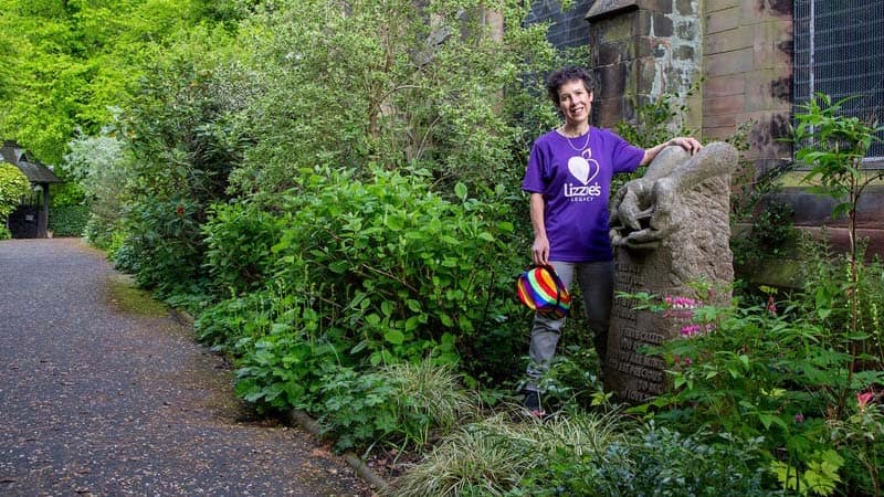 Hilary is standing in the grounds of St James church by a sculpture commissioned in memory of Lizzie. Carved in stone, it features a dove being carefully held in two cupped hands.