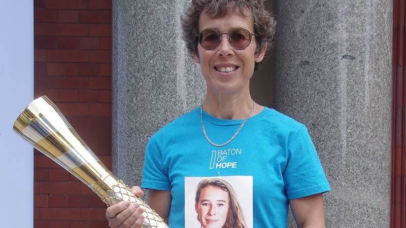 Wearing a blue Baton of Hope t-shirt, Hilary holds the gold and silver baton.